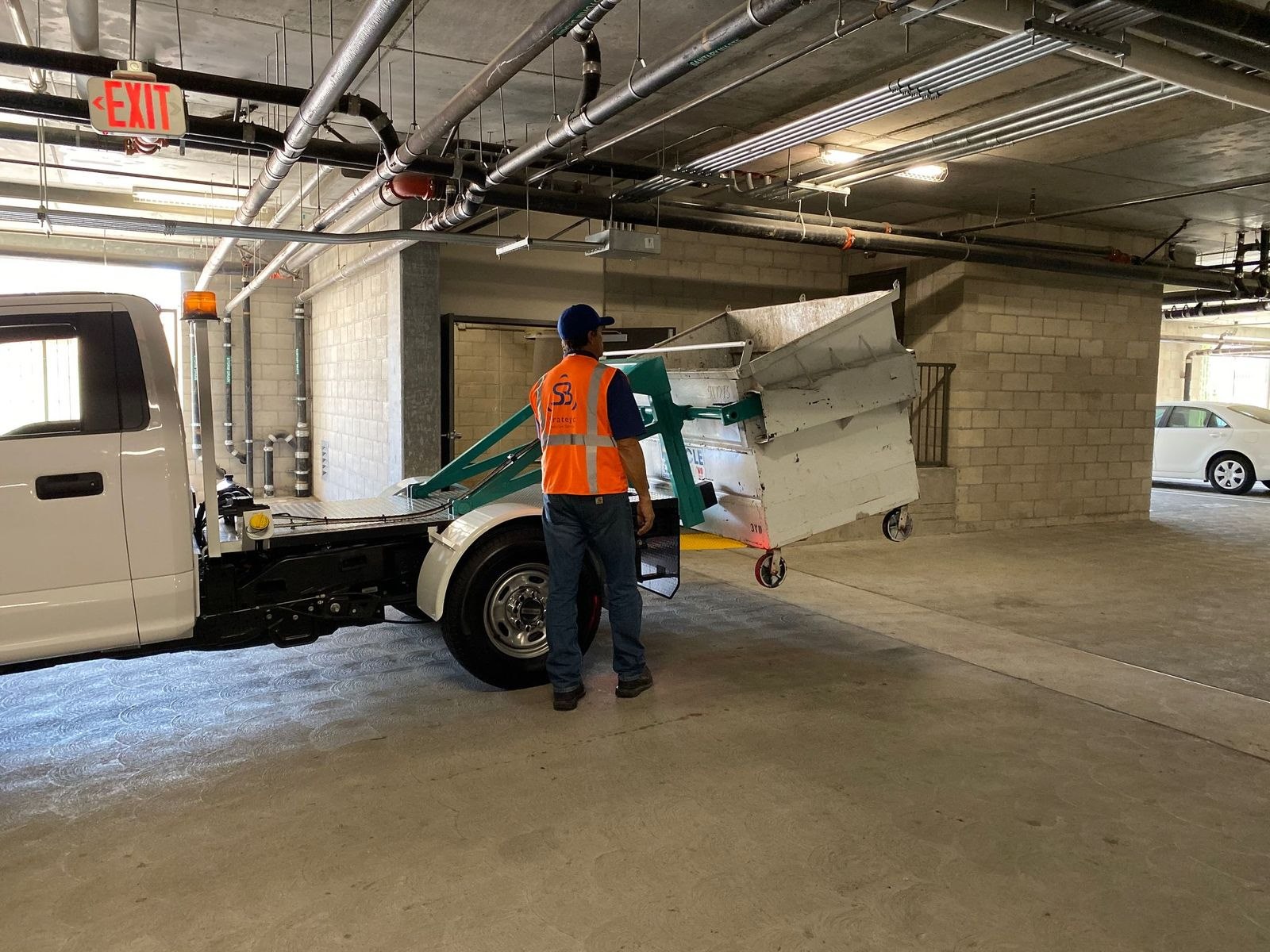 Strategic Sanitation technician positioning a large collection bin for transport inside a podium community garage
