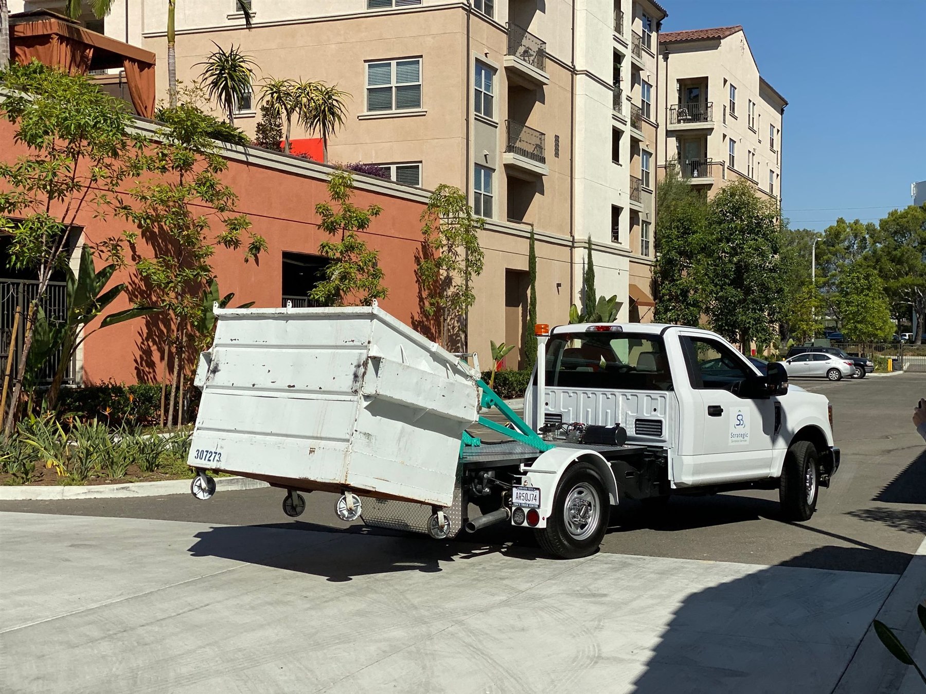 Strategic Sanitation truck transporting a large collection bin through a podium apartment community