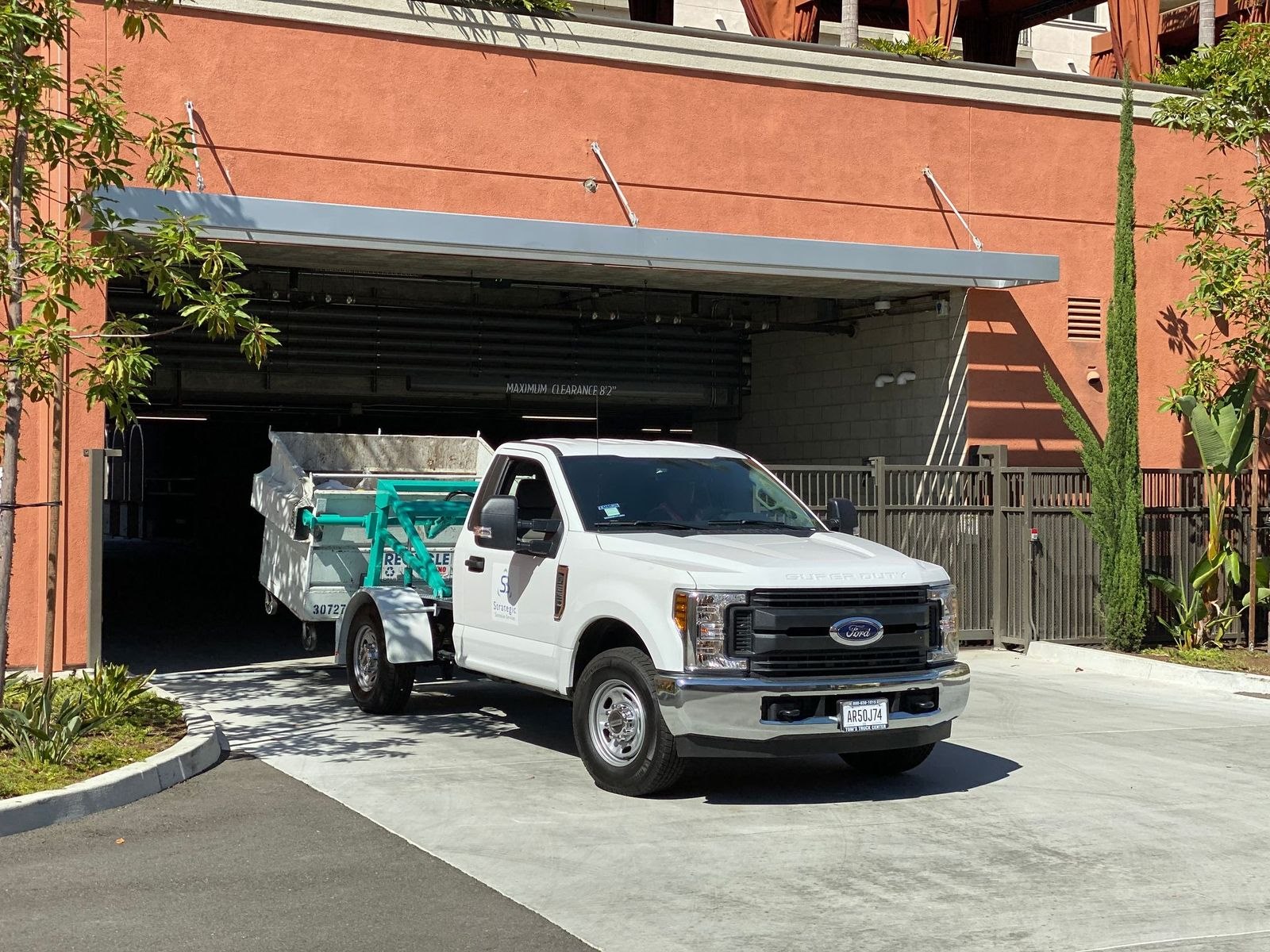 Strategic Sanitation bin transport truck moving a large collection bin from a podium community garage
