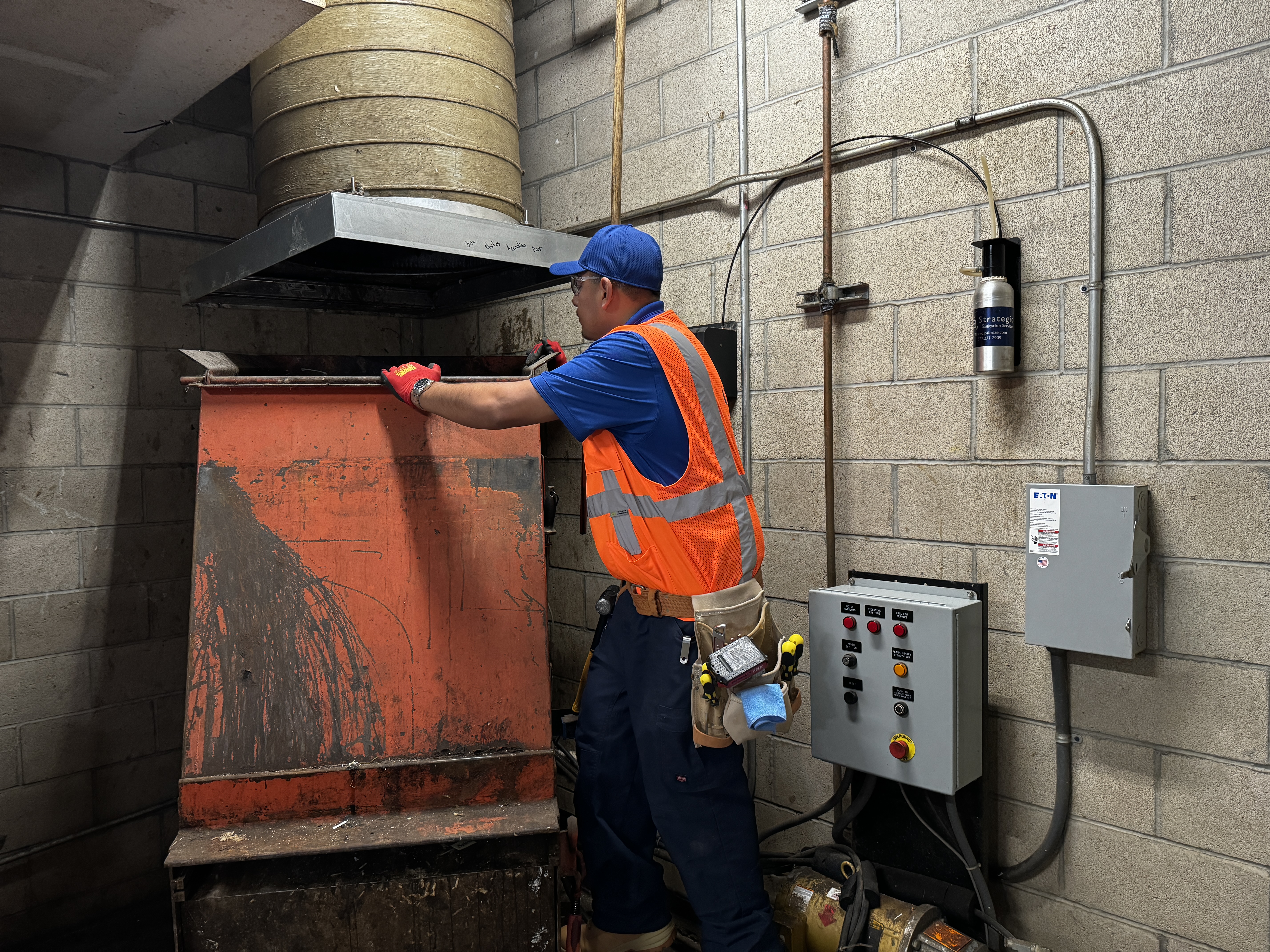 Strategic technician inspecting the compactor beneath a trash chute