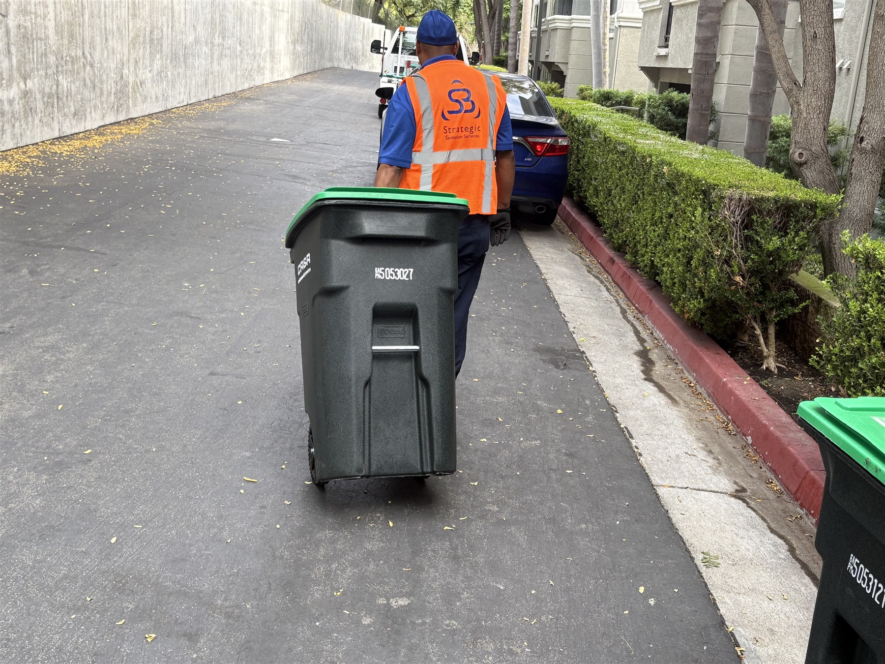 Strategic Sanitation technician transporting an organics tote through an apartment community