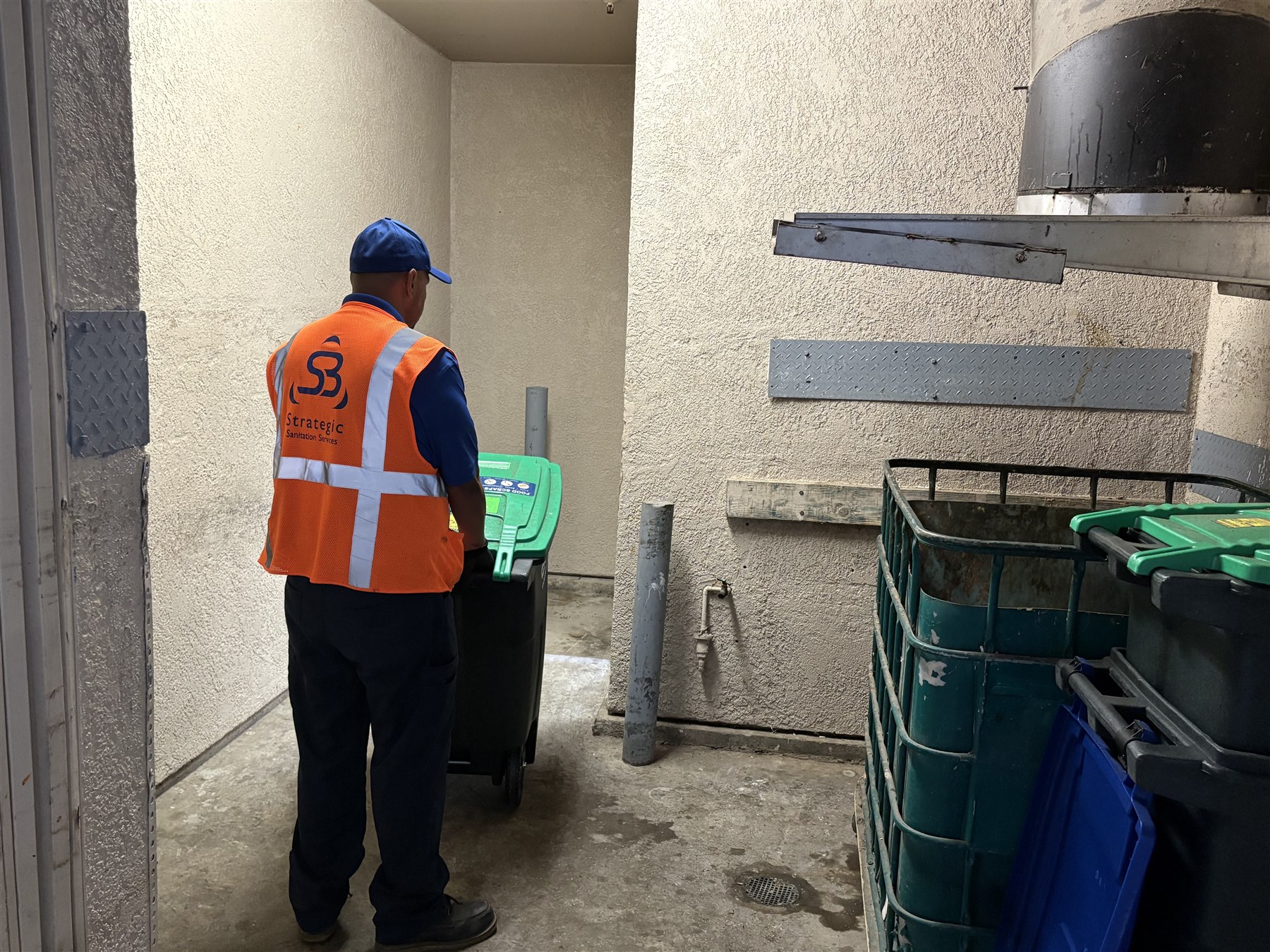 Strategic Sanitation technician transporting an organics tote through a multifamily trash area